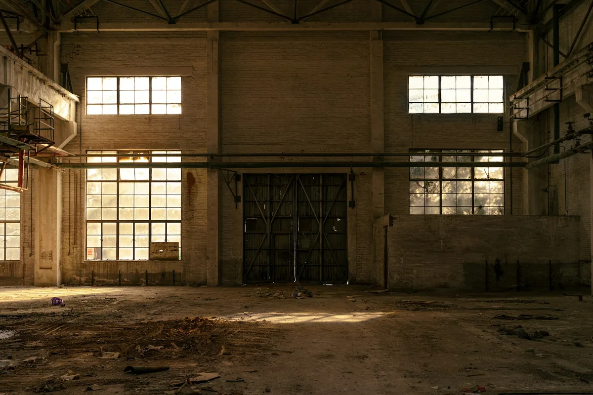 Empty industrial hall with tall windows and peeling paint, long abandoned