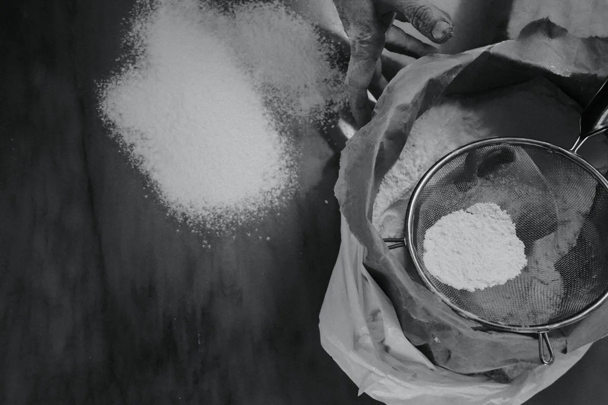 Hands sifting white flour through a metal sieve